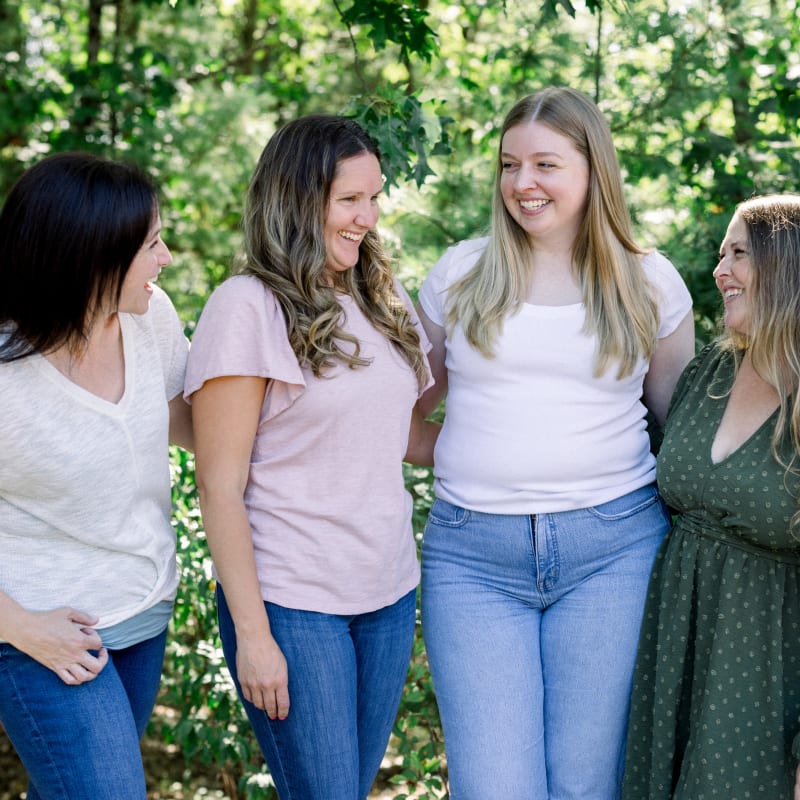Four adult woman are standing outside with their arms around each other. They are all smiling.