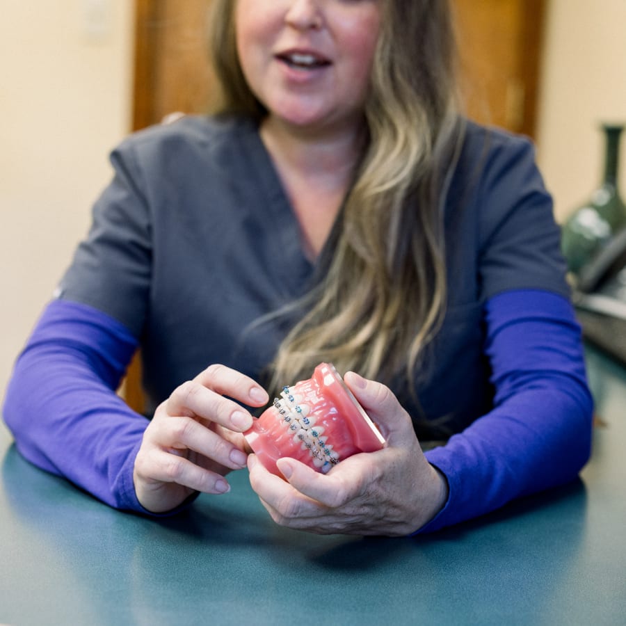 A dental professional shows off a model set of teeth with braces.