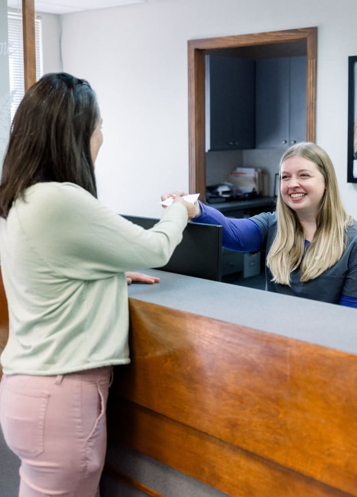 Receptionist talking to a patient and handing her a paper while smiling.