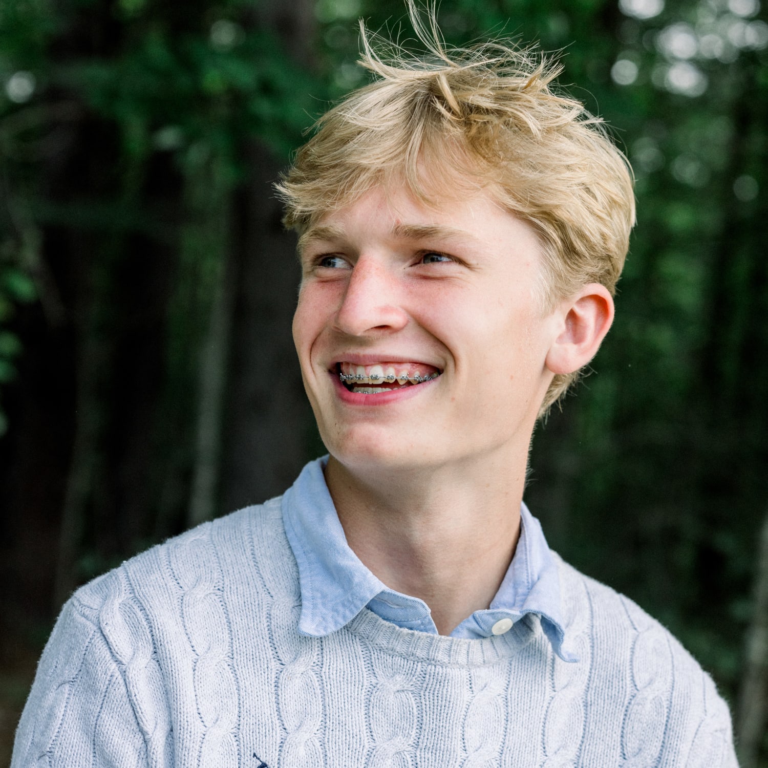 A teenage boy with blond hair is smiling and and showing off his braces.