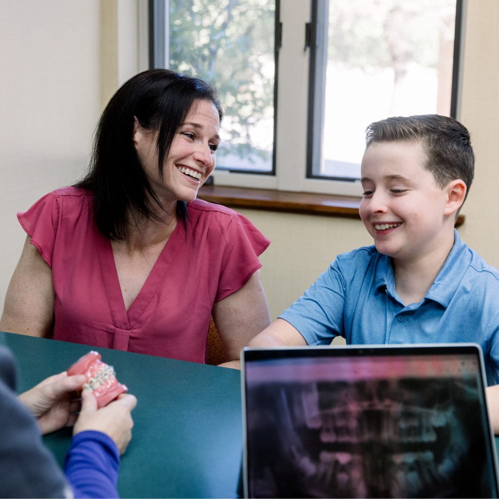 A mother and her son are sitting at a consultation table at All Star Smiles Orthodontics smiling.
