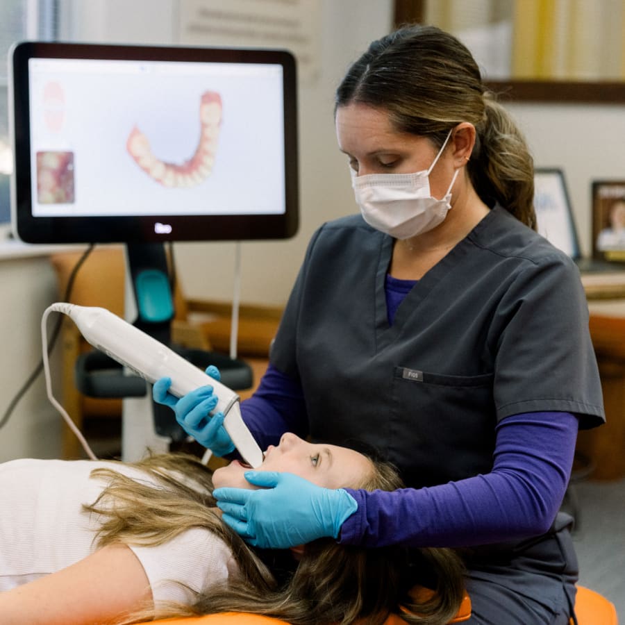 An orthodontic professional is using an iTero scanner to create a digital rendering of a young patient's mouth.