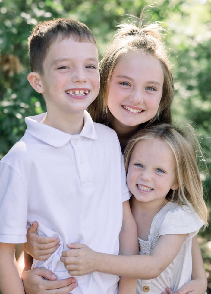 Three young people are smiling and hugging.