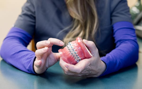 An orthodontist shows off a model of teeth wearing braces.