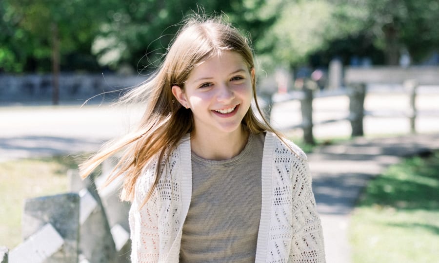 A young girl is standing outside and smiling.