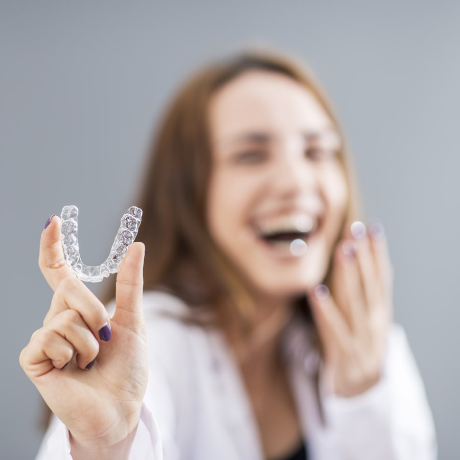 A woman holds up a set of Invisalign clear aligners.