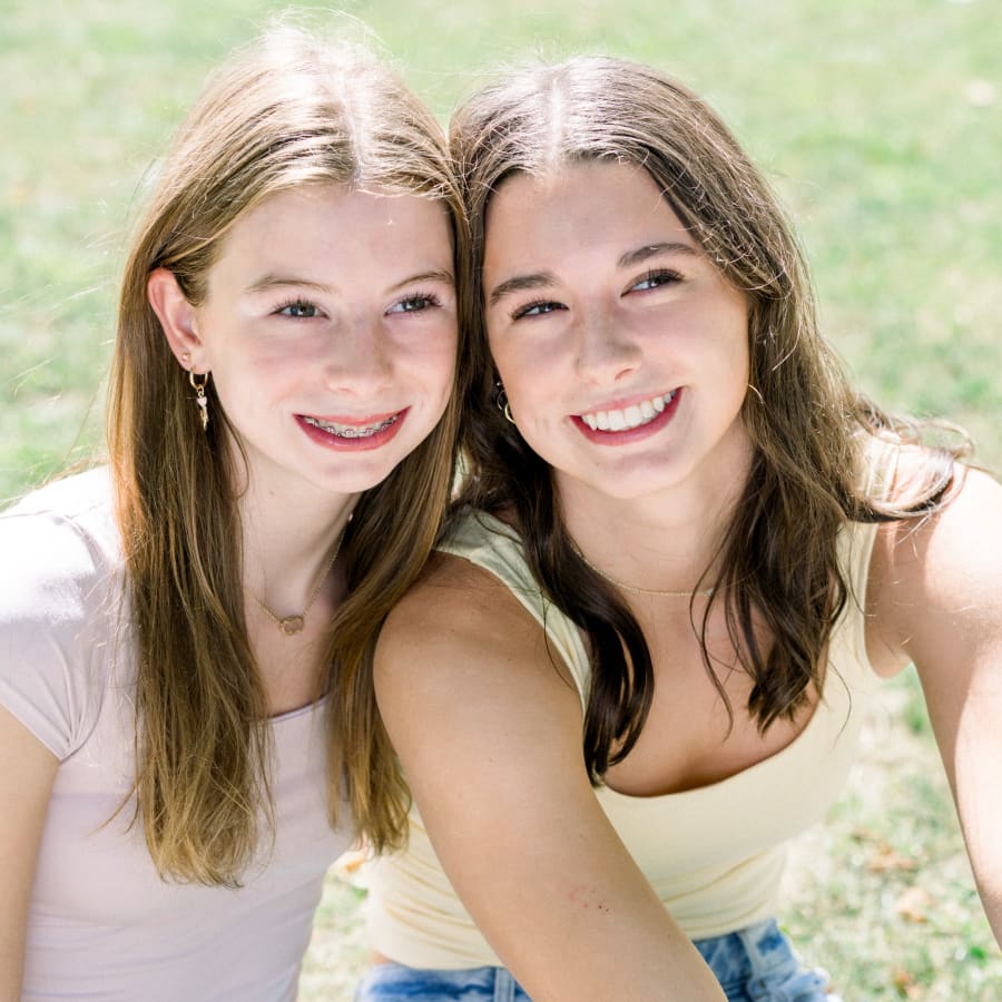 Two teen girls have their heads together and are smiling. One them has braces.