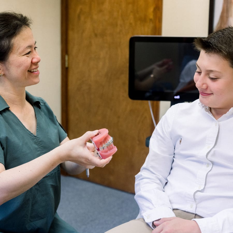 A teenage boy is talking to Dr. Diane. She is holding a model of a jaw with braces.